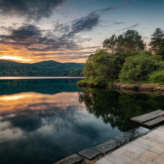 Create an image that depicts a serene, sunset-lit landscape. Imagine a tranquil lake surrounded by lush, green hills and tall, majestic trees. The sky is painted in shades of orange, pink, and purple, with the sun gently kissing the horizon. In the foreground, a wooden pier extends into the calm water, with a lone figure sitting at the edge, legs dangling over the side, enjoying the peaceful view. The water reflects the colors of the sky, creating a mirror-like effect. Add subtle details like gentle ripples in the water, a few birds flying in the distance, and soft, warm lighting to enhance the overall mood of tranquility and natural beauty. 